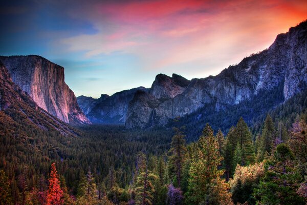 Une vallée d une beauté magique avec des nuances étonnantes de roches et une forêt multicolore au premier plan avec un ciel bleu-rouge