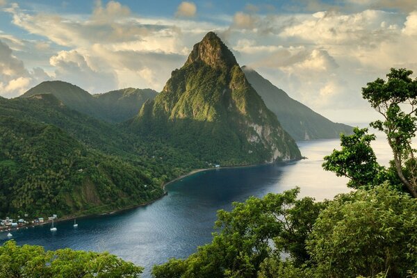 Blue river at the foot of green mountains, green trees on the right bank against the sky in white clouds