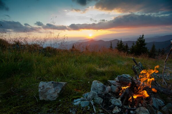 A bonfire lit against the backdrop of a beautiful mountain landscape with coniferous trees against the background of the setting sun