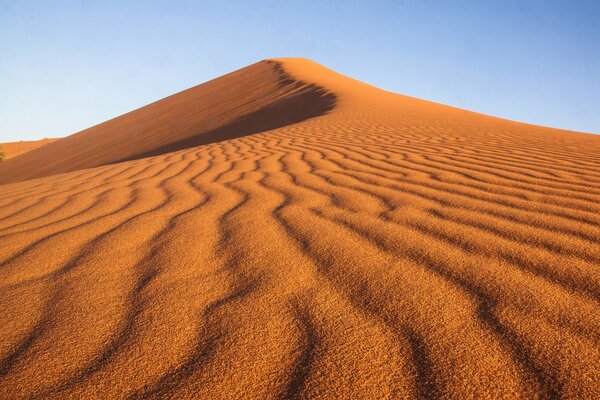 Désert avec un motif sur le sable en forme de lignes ondulées sur fond de ciel bleu