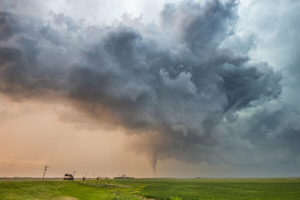 The tornado is moving. Stormy sky. There are people and cars on the road