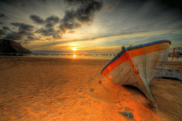 The boat lies on the seashore in the rays of sunset