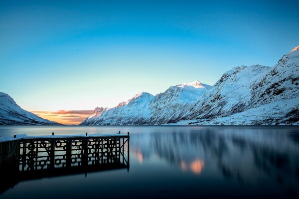 Muelle en el lago y montañas cubiertas de nieve