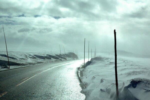 Light breaks through the clouds. Winter road with snow on the roadsides