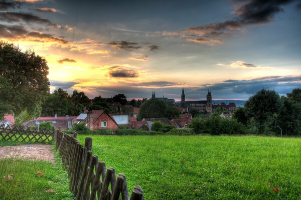 Hinter dem grünen Feld befindet sich ein kleines Dorf unter dem Himmel bei Sonnenuntergang