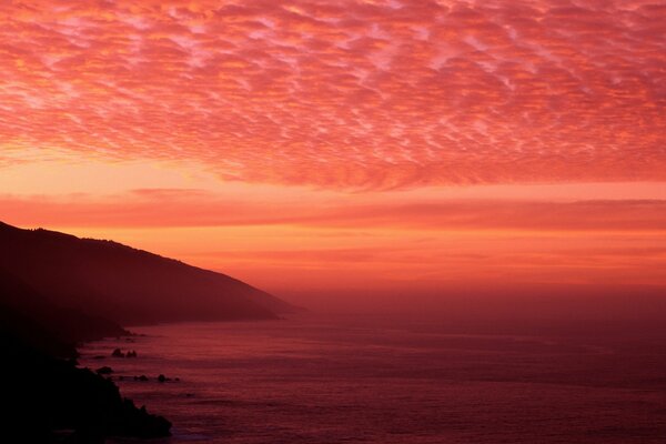 Tramonto cremisi sul mare con nuvole basse