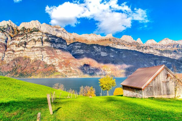 Holzhütte am See auf einem grünen Hügel mit riesigen Felsen