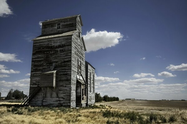 A barn in a field. There are clouds in the blue sky