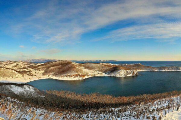 Blaues Meer auf dem Hintergrund der schneebedeckten Hügel