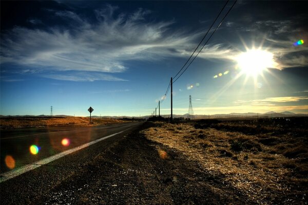 Route dans les prairies. Soleil. Beaucoup de poteaux le long de la route