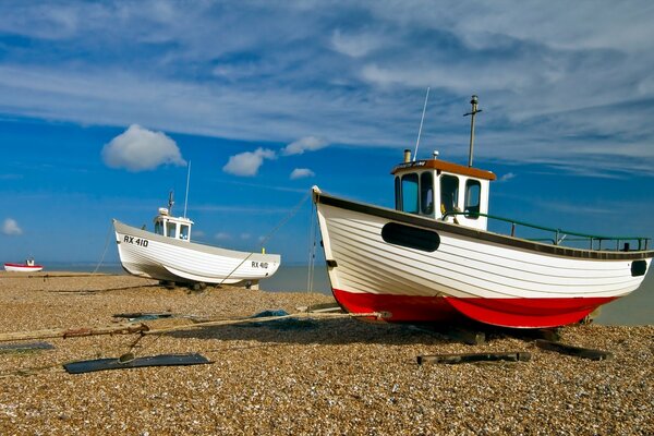 Boats on the shore of pebbles, blue sky with clouds