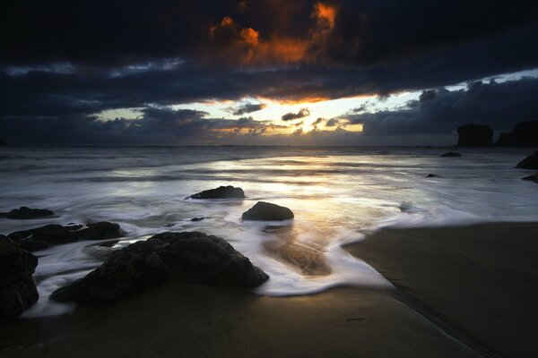 Puesta de sol en la orilla con piedras y nubes