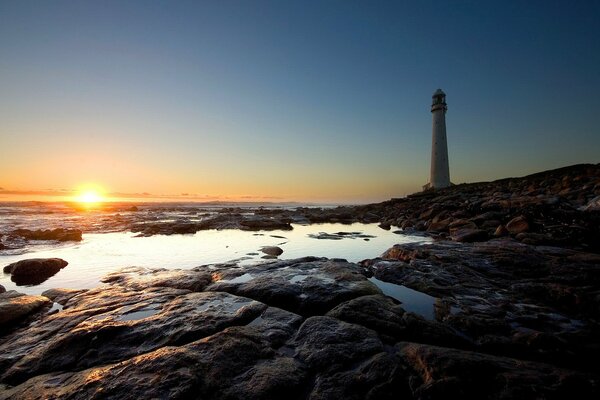 Phare au lever du soleil. Côte rocheuse au bord de la mer