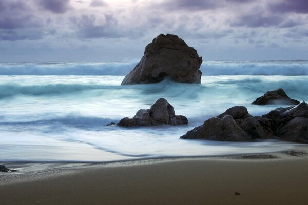 Foam waves break on rocks under a stormy sky