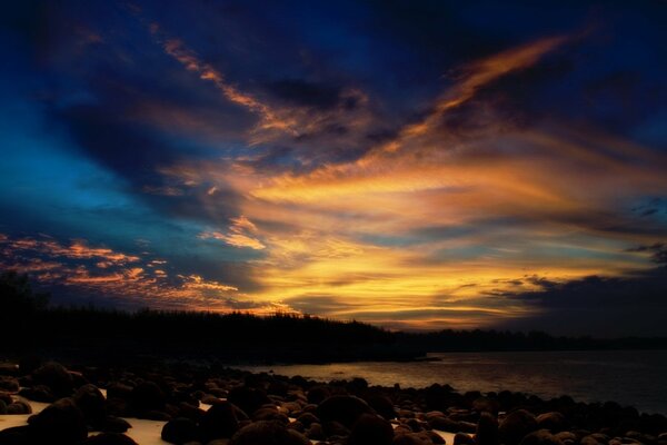 Puesta de sol en la orilla con piedras y nubes