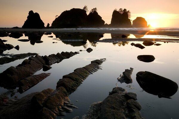 The sun rises from behind the rocks above the water