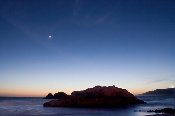 A rock in the sea at sunset in the moonlight