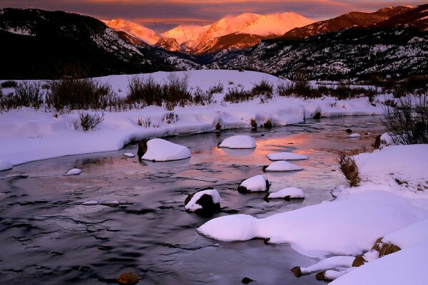Un río de invierno en las montañas con una puesta de sol en el fondo