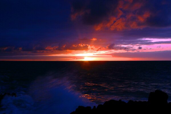 Die Welle bricht bei Sonnenuntergang über die Küste