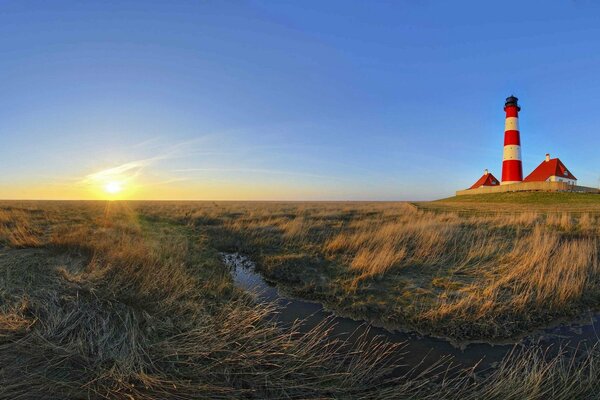 Dawn in the field against the background of a stream and a lighthouse