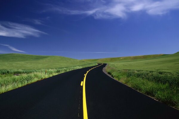 Bright yellow road markings on a background of green fields and bright blue sky