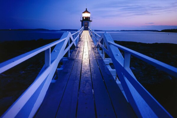 Lighthouse in the evening light at the end of a wooden bridge