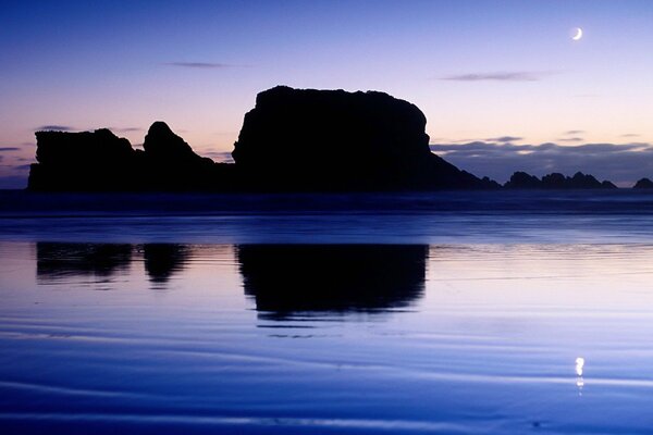 Las rocas se reflejan en el agua en el fondo de la puesta de sol