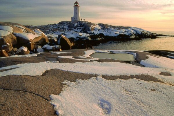 The lighthouse is covered in snow, there are people next to the lighthouse