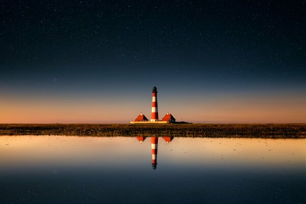 Ein Leuchtturm in der Ferne spiegelt sich im Wasser wider