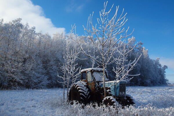 An abandoned tractor near a snow-covered forest