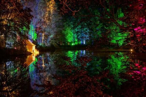 Las luces multicolores se reflejan en el estanque. Casa en la orilla del estanque