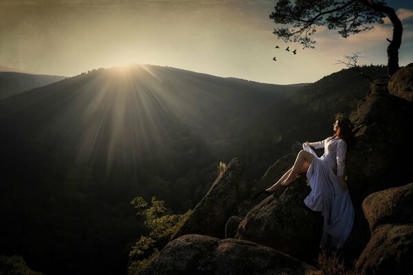 Девушка на камнях в горах на фоне заходящего солнца