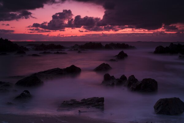 Tramonto rosa nella nebbia del mare tra le pietre