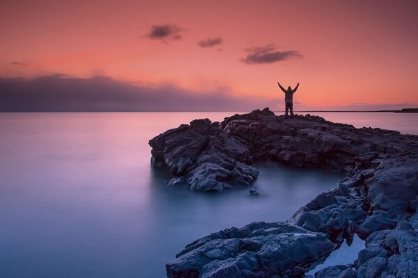 Hombre en la orilla rocosa del mar al atardecer