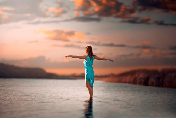 La chica está de pie en el agua. Hermosa foto de puesta de sol