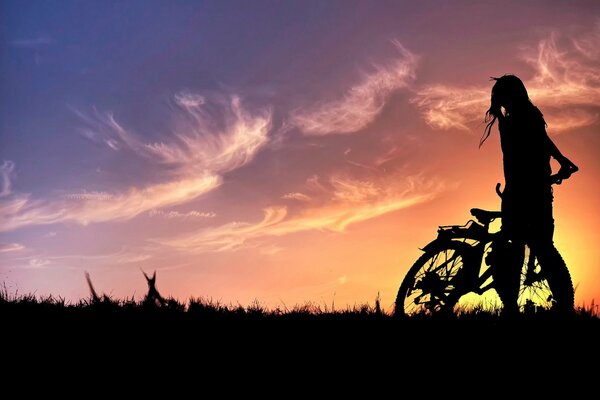 Silhouette eines Mädchens mit einem Fahrrad bei Sonnenuntergang