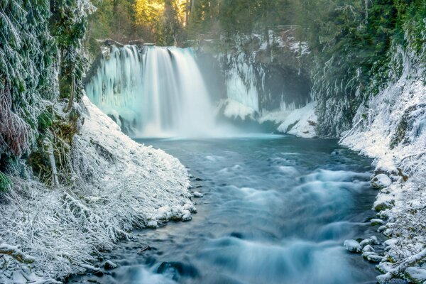 Winter river with a waterfall between snow-covered trees