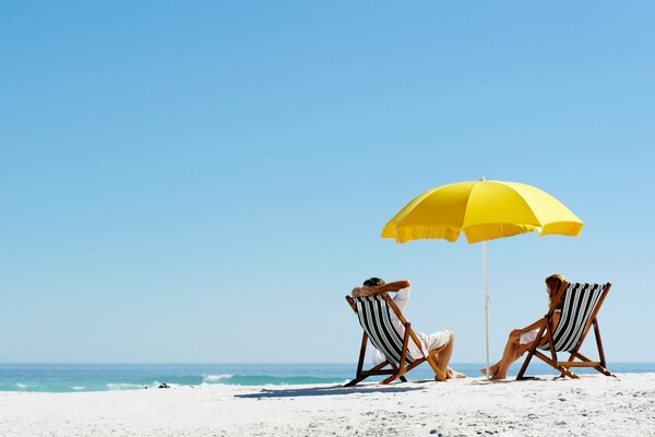 Two people are sitting in sun loungers on the beach