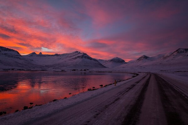 Winter road along the lake on the background of sunset