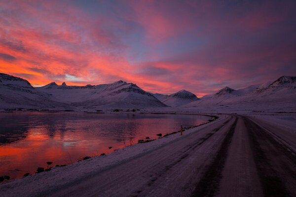 Camino de invierno a lo largo del lago en medio de la puesta de sol