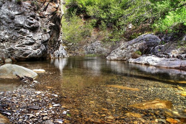 Sauberes Wasser mit Kieselsteinen auf dem Hintergrund hoher Felsen