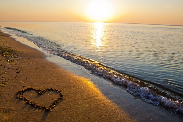 Cuore sulla sabbia sullo sfondo del tramonto del mare