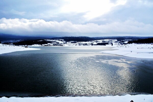 A beautiful winter lake with snow-covered shores under the rays of the sun