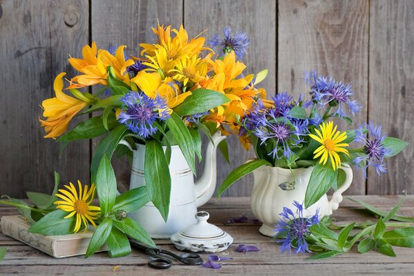 Blumenstrauß aus Lilien und Kornblumen am Tisch mit Schere und Buch