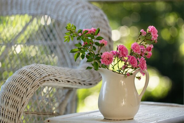 Pink flowers in a jug on the table by the chair