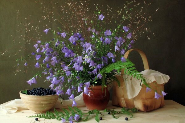 Still life of a bouquet of bluebells a basket and blueberries in a plate