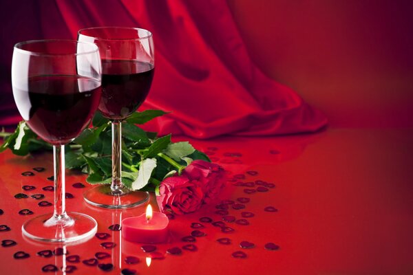 Два бокала красного напитка и две розы на красном фоне