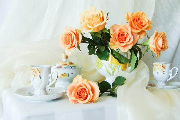 Still-life. A bouquet of roses and a tea set on a snow-white tablecloth