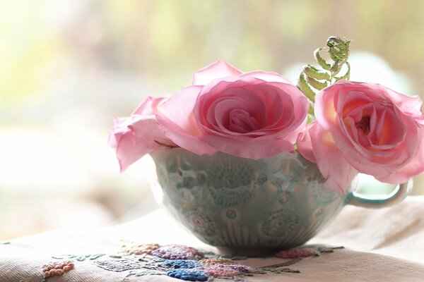 Tasse mit Rosen in der Nähe einer bestickten Serviette