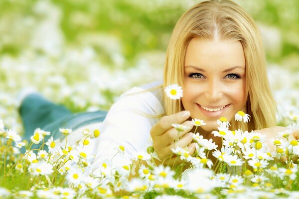 Blonde girl on the field with daisies smiles